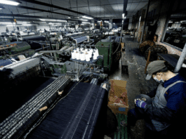 Xintang, the Blue Jeans City. A worker supervises a power loom weaving denim to be used to manufacture blue jeans in LSH textile company, in Xintang, Guangdong province, China, on February 9, 2012. Photo by Lucas Schifres/Pictobank. Public Domain.